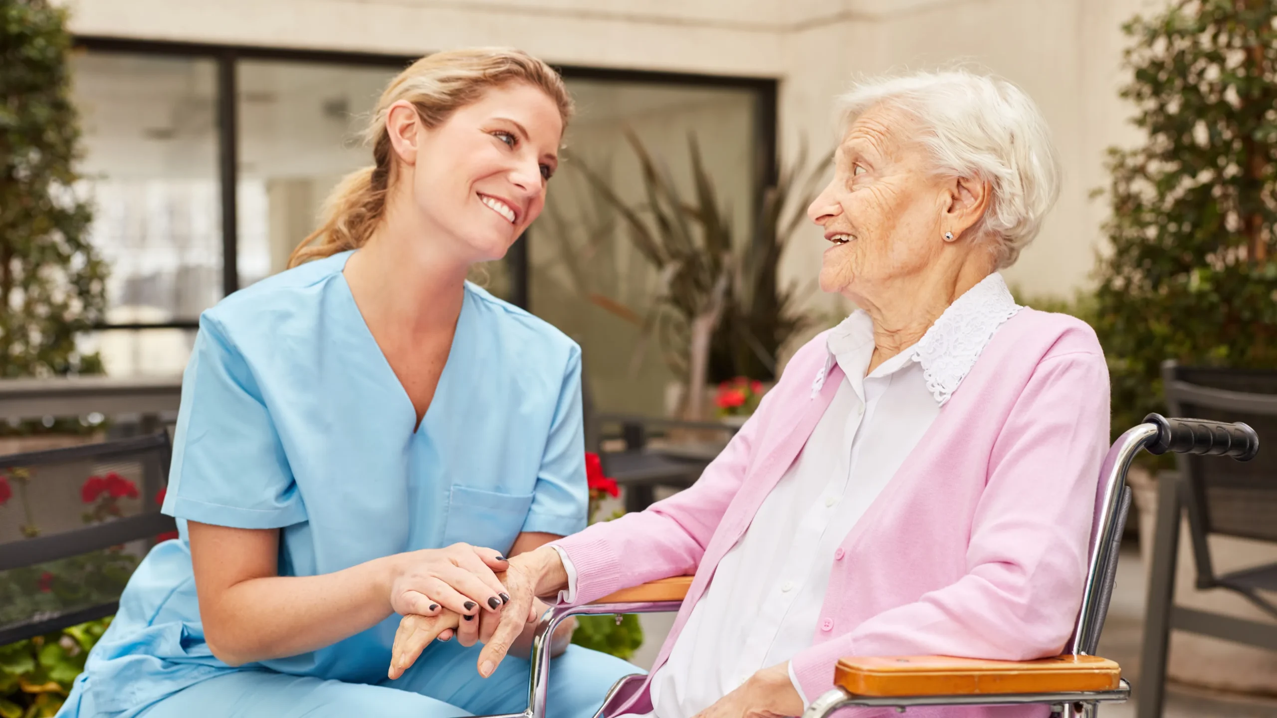 Caregiver holding hands with elderly woman in wheelchair