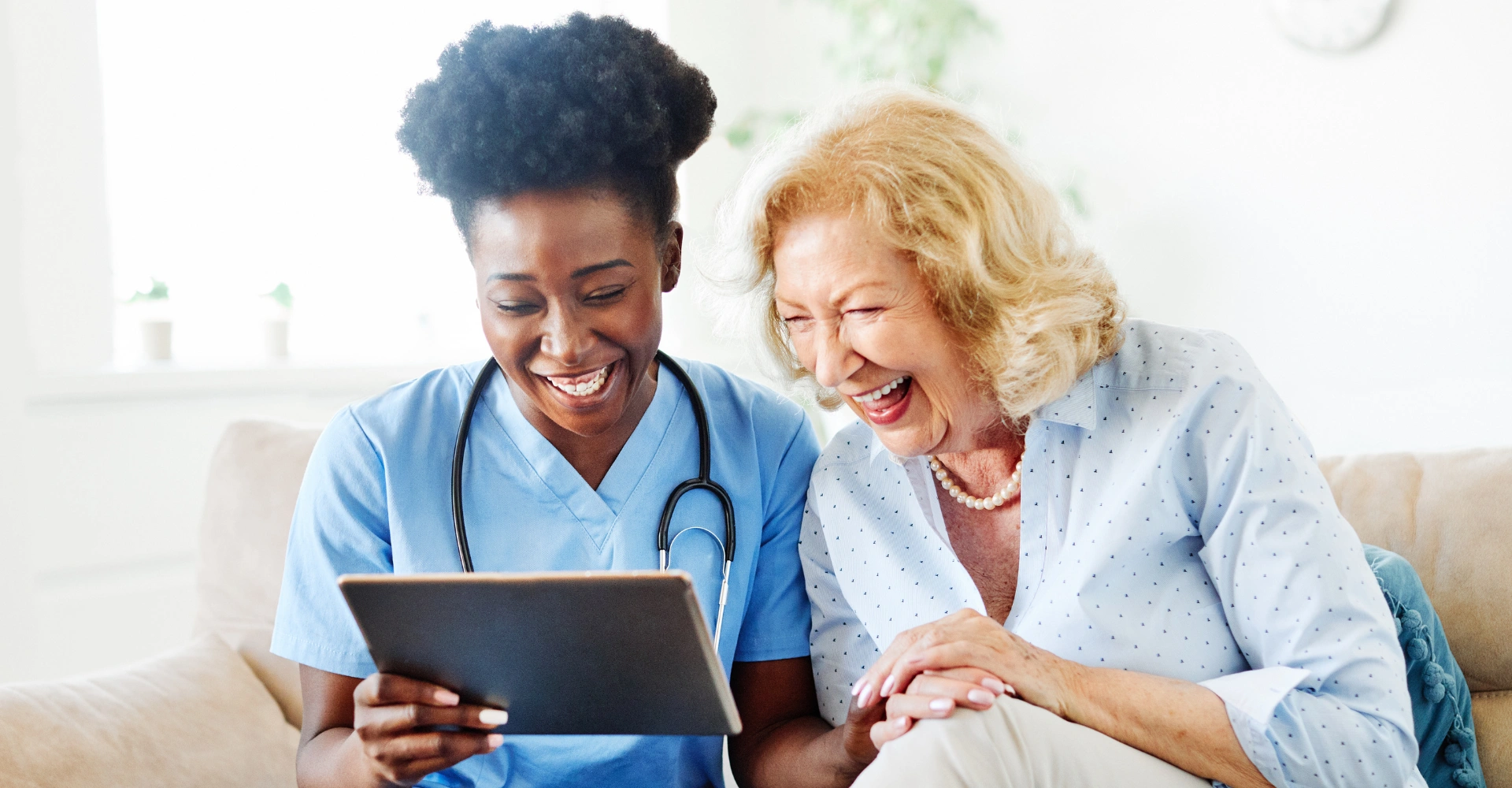 Nurse and senior woman laughing over tablet