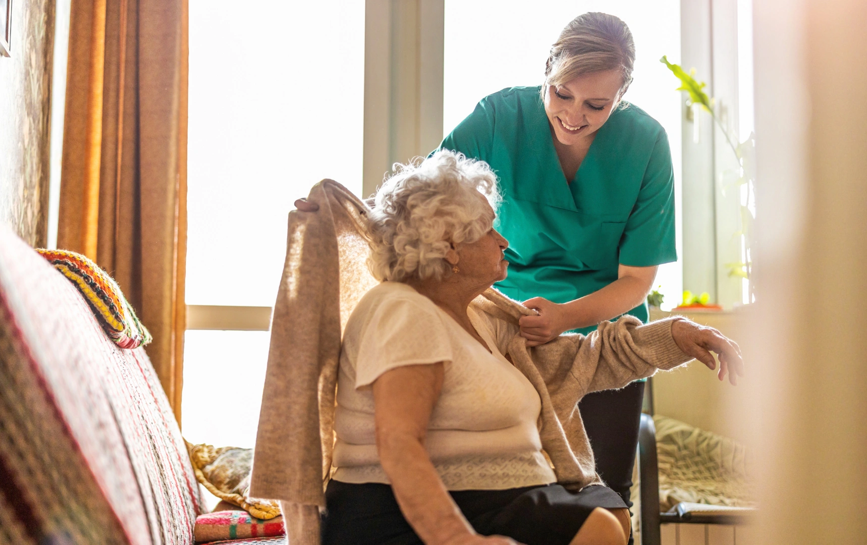 Caregiver helping elderly woman put on cardigan