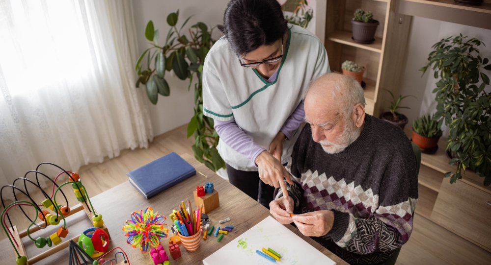 Caregiver assisting elderly man with arts and crafts