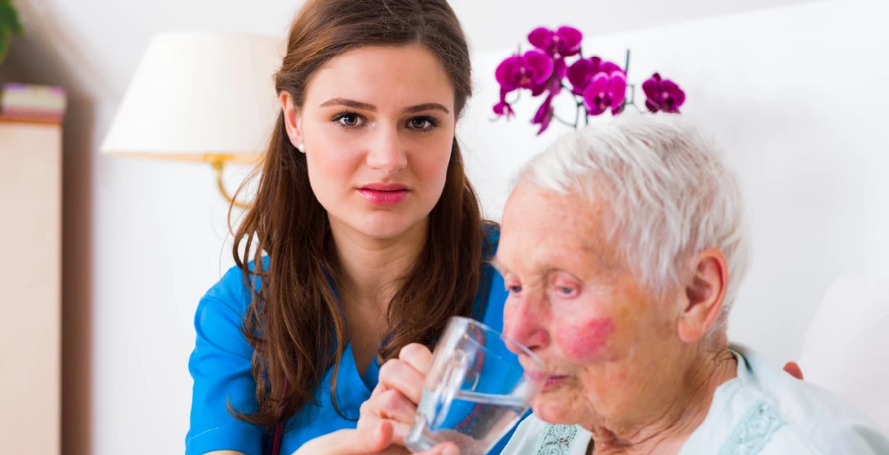 Caregiver helping elderly woman drink water