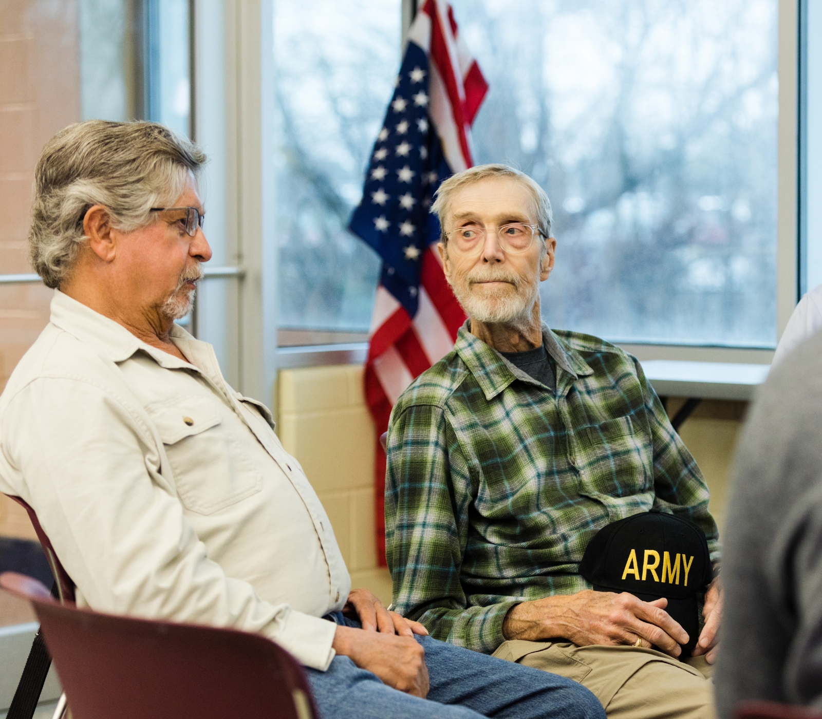 Two older men seated, one holding Army hat