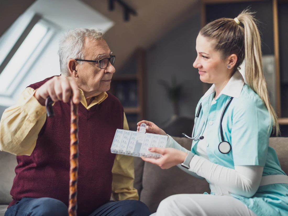 Nurse giving pill organizer to elderly man