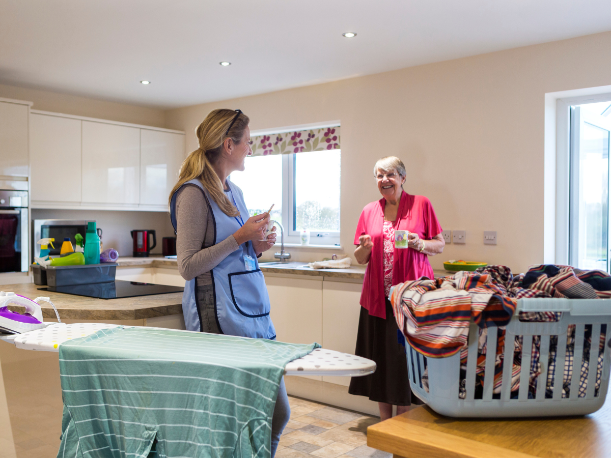 Caregiver and elderly woman chatting in kitchen