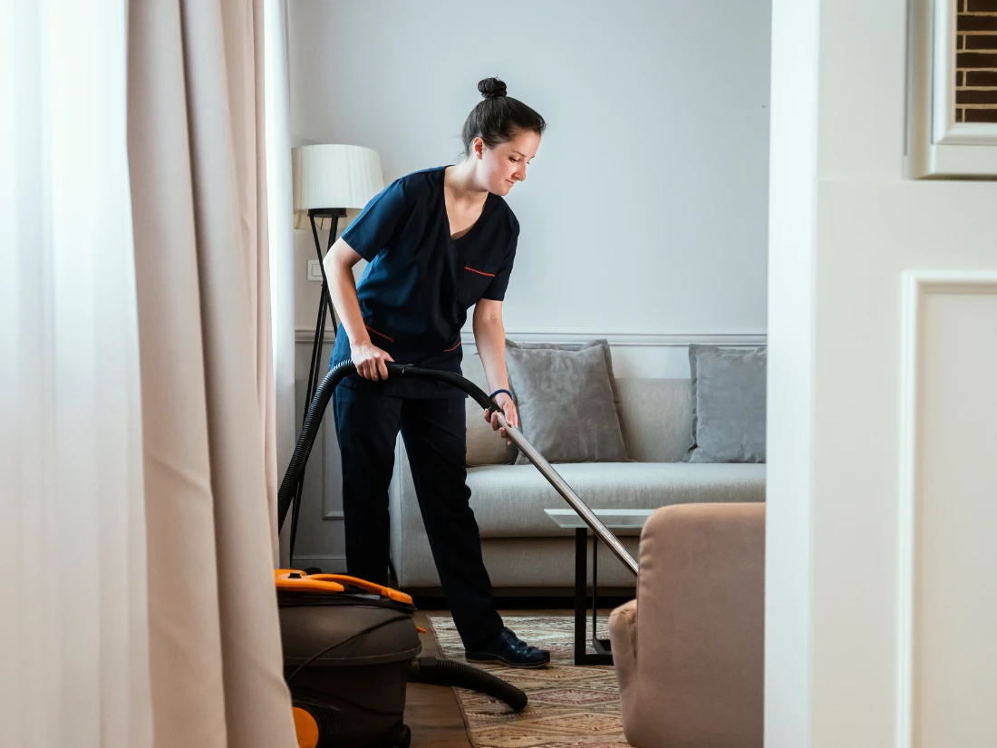 Cleaner vacuuming living room carpet