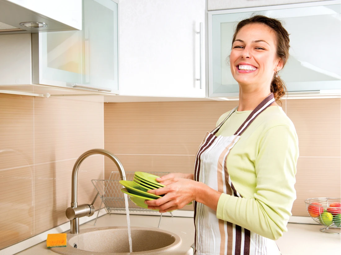 Smiling woman washing dishes at kitchen sink