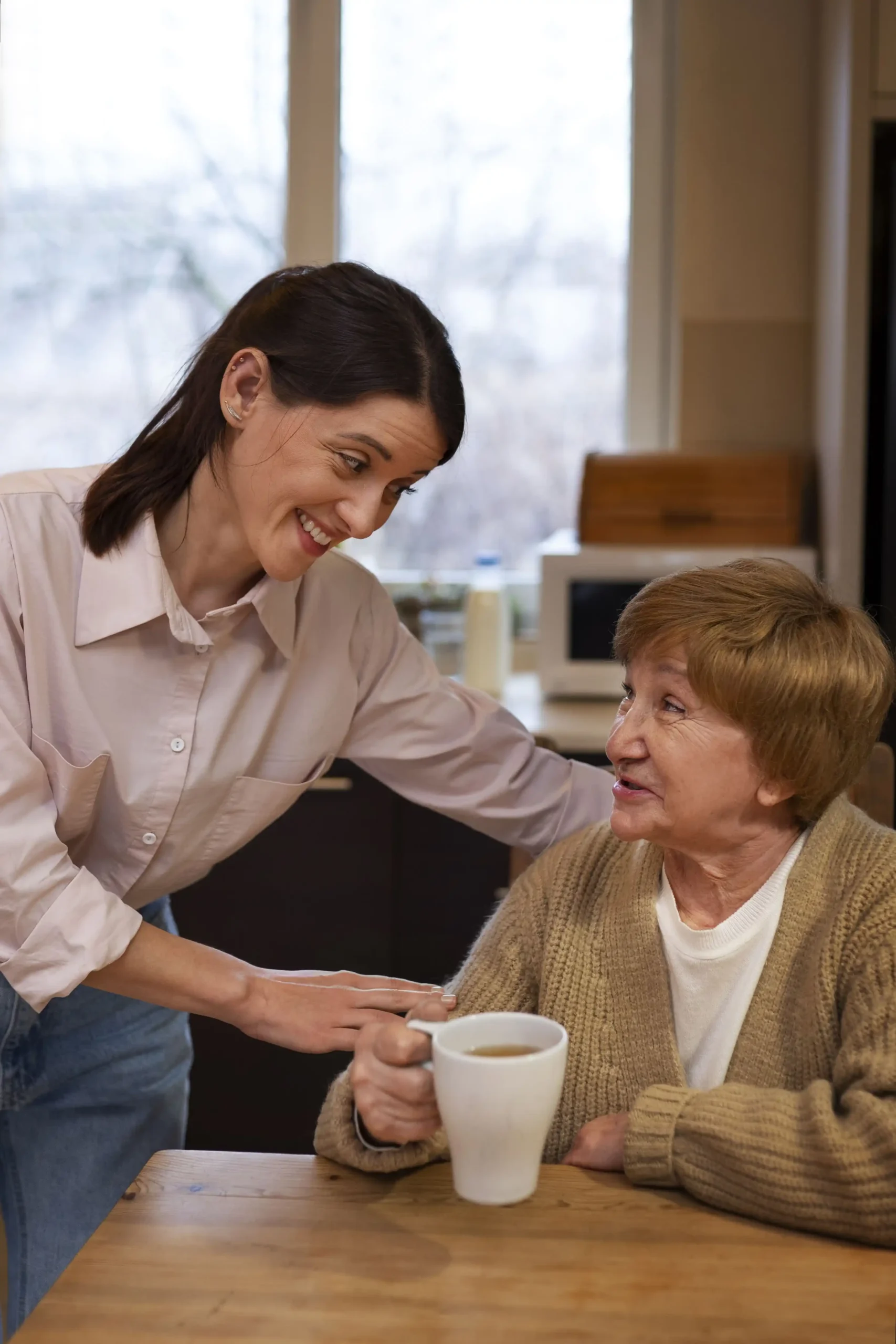 Caregiver offering coffee to elderly woman