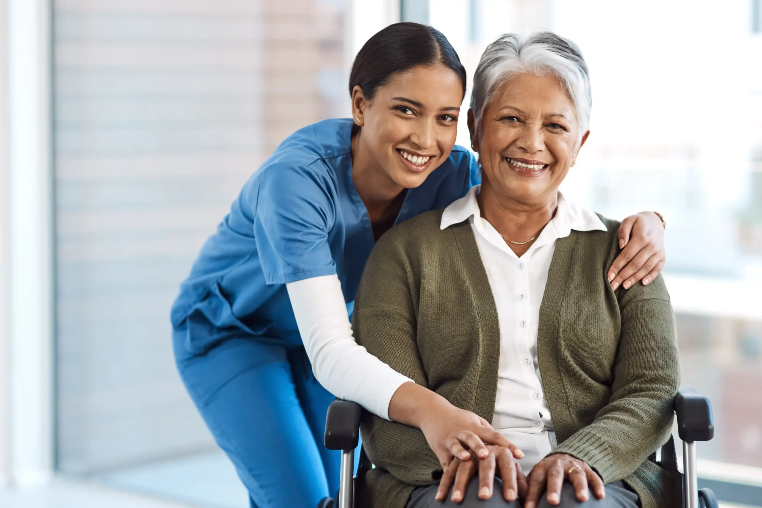 Caregiver hugging smiling senior woman in wheelchair